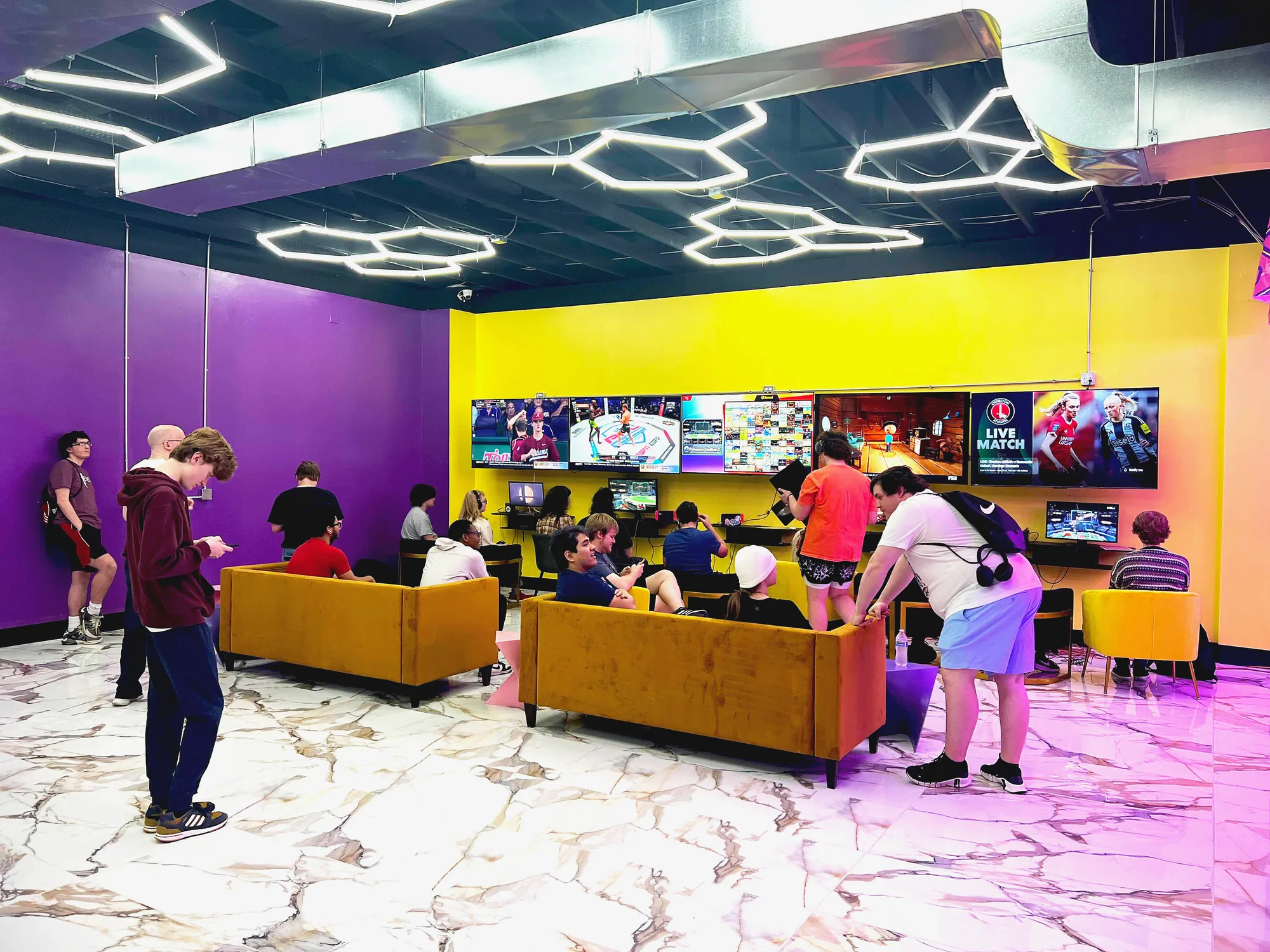 Lounge with orange sofas, yellow wall and a wall of screens